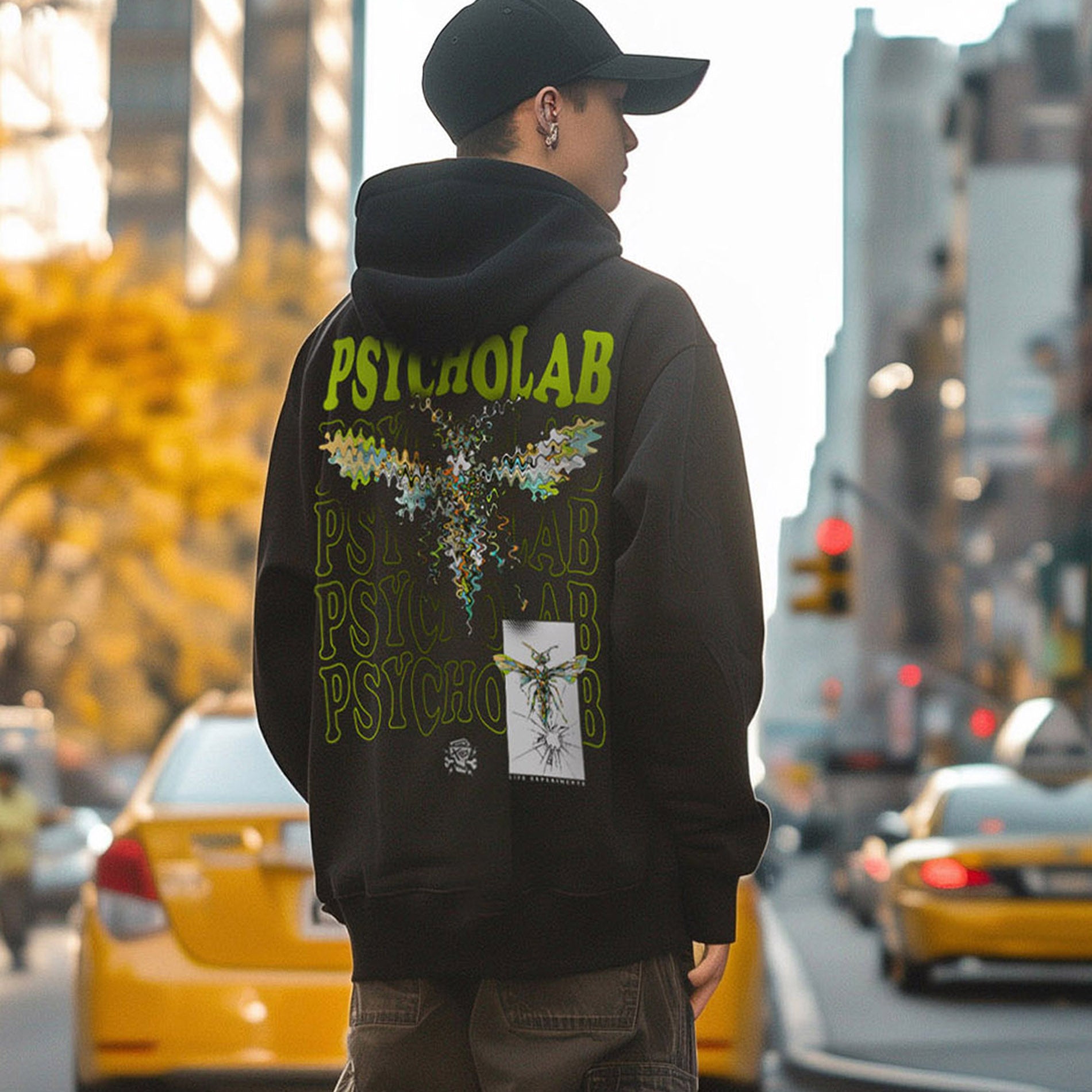 Hoodie Anamorphic von PsychoLab, auffälliges grünes Design auf der Rückseite, urbaner Stil in einer Stadtlandschaft mit gelben Taxis im Hintergrund, perfekt für kreative Streetwear fans.