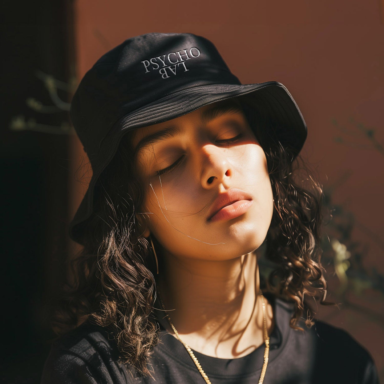 Junge mit lockigen Haaren trägt den PsychoLab Bucket Hat Reversed in Schwarz, der ein umgedrehtes weißes Logo zeigt, ideal für den Streetwear-Look. psycholab